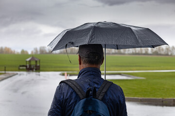  a man stands under an umbrella in rainy weather.