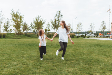 Mother and daughter play and run around the park on a beautiful day. the family is having fun in the park on the grass. morning jog.