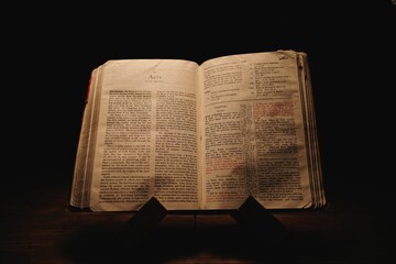 Closeup shot of a historic old Bible open on the Acts pages on display in a dark room