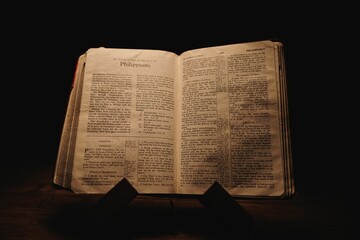 Closeup shot of a historic old Bible open on the Philippians pages on display in a dark room