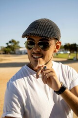 Naklejka premium Portrait of young handsome Caucasian male with glasses and cap and toothpick in the mouth on beach