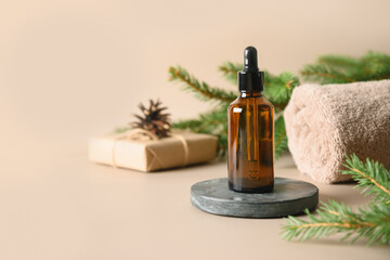 Naklejka premium Christmas Spa concept with cosmetic aroma oil, pine cones, evergreen branches on beige background. Winter holiday for body care and wellness. Vertical format. Close up.
