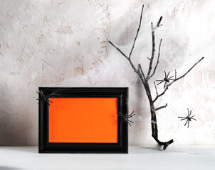 Hallowen minimal image. Black frame with orange empty space for text, spiders, dry twig in cobwebs.