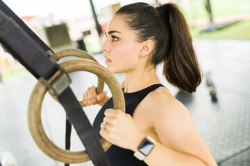 Side view of a strong woman practicing row back exercises with rings