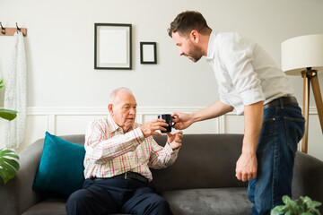 Young son bringing coffee while chatting with his old senior father
