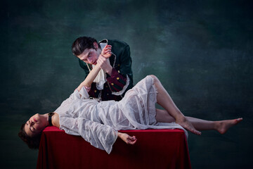 Portrait of man in image of vampire biting hand of young woman lying on table over green background. Blood drinking - obrazy, fototapety, plakaty