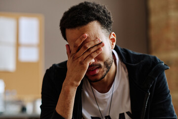 Young depressed man touching face while suffering from post traumatic syndrome and describing his...