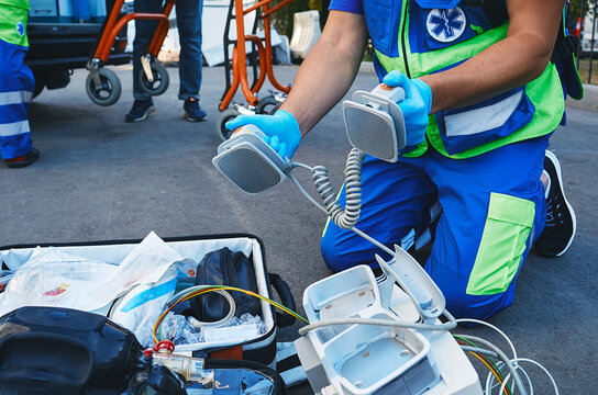 Ambulance Paramedic Holding Defibrillator Pads In Hands While Resuscitation Casualty Outdoors Near Ambulance. Performing First Aid