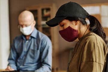 Side view of young upset woman in protective mask and baseball cap sharing her traumatic experience with support group at session
