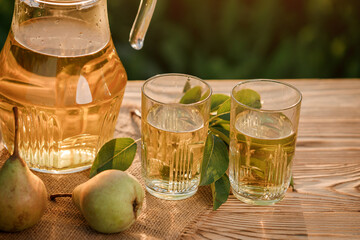 Two glasses with pear juice and basket with pears on wooden table with natural orchard background on sunset light. Vegetarian fruit composition