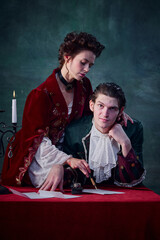 Portrait of man and woman in medieval costumes over dark green background. Writing mysterious story about vampires