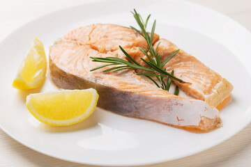 Salmon served with rosemary, fresh lemon on white dish. Healthy eating. Mediterranean cuisine. Pescetarianism.