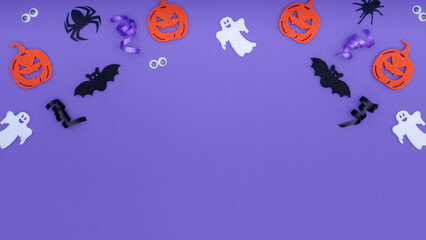 Halloween decorations on purple background. Happy Halloween concept with copy space. Border made from pumpkins, bats, ghosts, spiders and eyes on a purple backing.