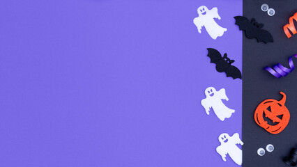 Halloween decorations on purple background. Happy Halloween concept with copy space. Flat lay border composition made with pumpkins, bats silhouettes, eyes and pumpkins.