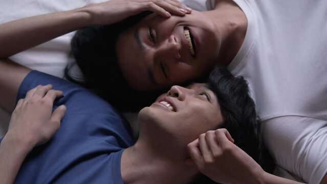 Young Asian gay couple lying on bed in a romantic mood together spending quality time at home. LGBT couple in a relationship showing love and affection while together.