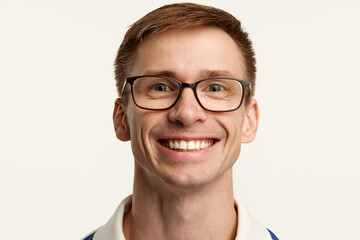 Fototapeta premium Portrait of young man in glasses cheerfully smiling, looking at camera, posing isolated over white studio background