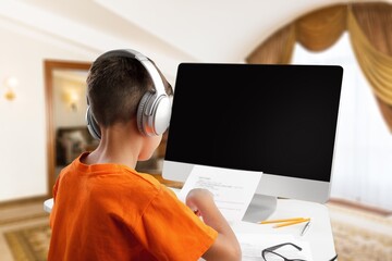 Child in headphones studding on a computer at room