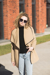 Fototapeta premium Portrait of a young Caucasian girl in a coat and sunglasses in the city on an autumn day.