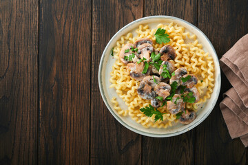 Fusilli pasta with mushrooms, cheese and garlic creamy sauce on plate on old wooden dark table background. Top view. Traditional Italian cuisine.