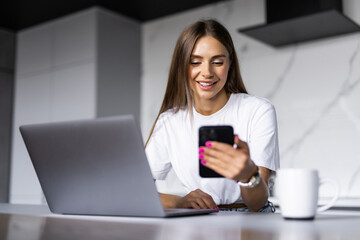 Young woman use laptop to work in the kitchen hold the phone