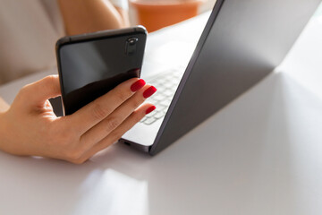 close up, a woman holds a smartphone in her hand and sits at a laptop. Online shopping concept