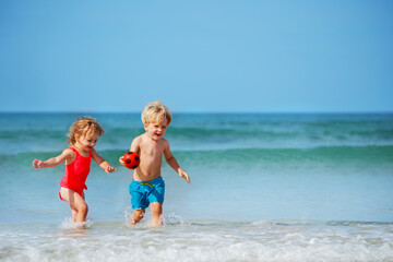 Boy and sister girl run on the sand beach smiling over sea waves