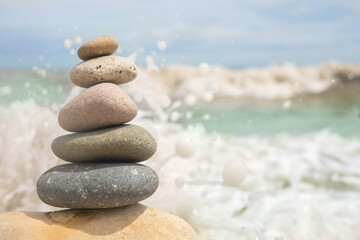 Pebble tower on sunny beach sea wave splashing water balance pyramid harmony peace of mind
