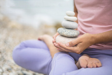 Yoga woman hands holding pebble tower sitting lotus position meditation balance harmony closeup