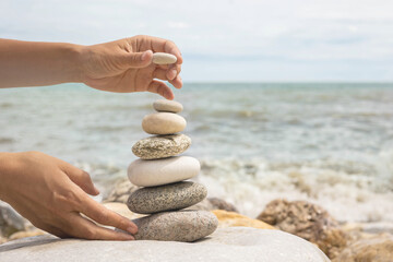 Relaxed spiritually woman hand arrangement pebble tower cobblestone sea coastline landscape closeup