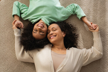 top view of smiling african american girl lying on carpet with cheerful mother.