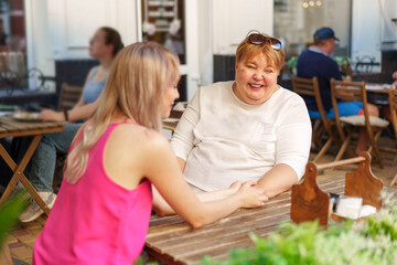 Obraz premium Mother with disability in wheelchair talking to her daughter while sitting at the table in cafe