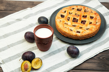 shortbread cookies with plums and a glass of milk on a wooden table. concept of homemade shortcrust pastry. baked fruit dessert on the kitchen table with a drink close up