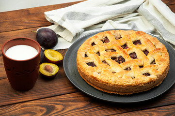 shortbread cookies with plums and a glass of milk on a wooden table. concept of homemade shortcrust pastry. baked fruit dessert on the kitchen table with a drink close up