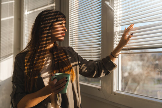 Woman holding a cup looking through the window