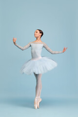 Portrait of tender young ballerina dancing, performing isolated over blue studio background. Standing on pointe