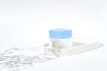 Plastic jar with face cream on concrete tray. White background with daylight and beautiful shadows. Skincare products, natural cosmetic. Beauty concept for face and body care