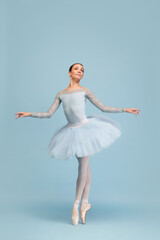 Naklejka premium Portrait of tender young ballerina dancing, performing isolated over blue studio background. Beauty of classical dance