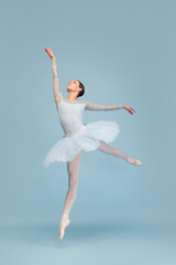 Portrait of tender young ballerina dancing, performing isolated over blue studio background. Lightness and grace