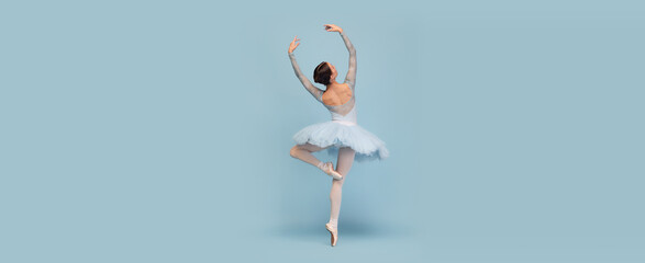 Portrait of tender young ballerina dancing, performing isolated over blue studio background. Flyer image - obrazy, fototapety, plakaty