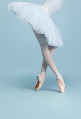 Cropped image of female legs, ballerina in tutu and pointe standing on tiptoe isolated isolated over blue studio background - obrazy, fototapety, plakaty
