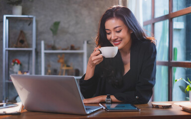 A asian female freelance is drinking coffee while working in cafe by laptop or notebook feeling relaxing. Businesswoman is working online job in coffee shop. Concept of new normal lifestyle. 