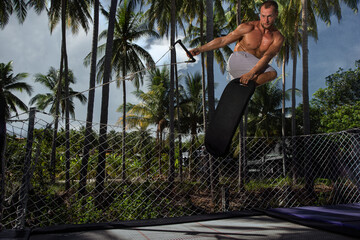  A man is engaged in trampoline jumping on a rubber board against a tropical background