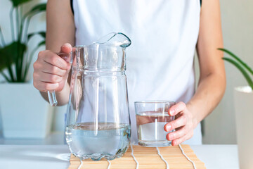 Close-up of female hands holding glass and jug of clean drinking water, morning rituals for women's health. The concept of healthy lifestyle