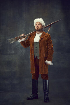 Nobleman, medieval royal person in vintage hunting clothing with old gun isolated over dark background. Art, fashion, emotions, traditions, hobby concept