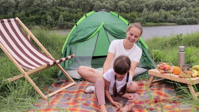 Caucasian young adult woman wearing white t shirt spending time in nature with her cute daughter, little girl laughing while her mother tickling her.