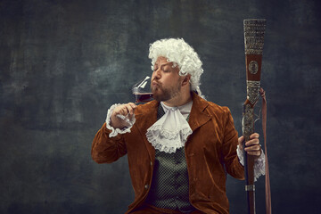 Drinking wine. Vintage portrait of young man in brown vintage suit and white wig like medieval...