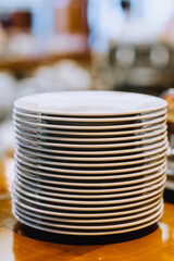 A lot of white clean round empty plates stand in a row on a wooden kitchen table.