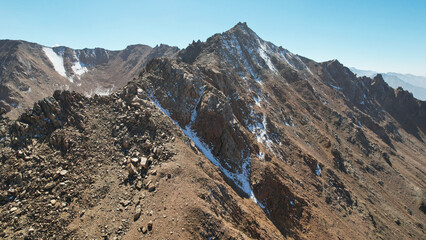 A rocky pass overlooking the snowy mountains. Steep cliffs and big rocks. Blue clear sky. The peaks of the mountains are covered with snow. Top view from a drone. Traces of loose stones. Kazakhstan