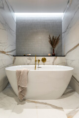 Modern bathroom interior with design marble floor, bathtub, towels, dried flowers in vase and...