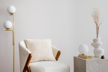 Warm and cozy living room with design white armchair, gold lamp, marble cube, vase with dried...